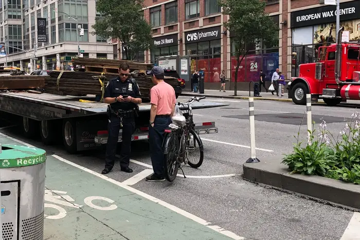 An NYPD officer tickets a cyclist on 6th Avenue just north of West 24th Street, where bike messenger Robyn Hightman was killed by a hit and run truck driver last month.